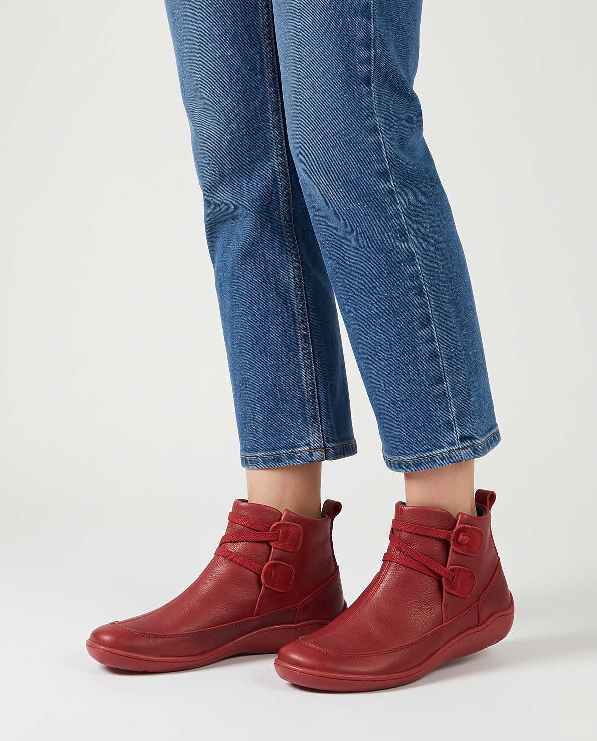 Women's soft leather ankle boots with a criss-cross strap and two button tabs on the side, back pull tab and flexible wavy sole in Red, front view