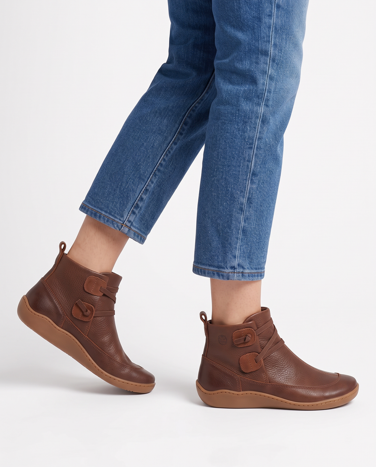 Women's soft leather ankle boots with a criss-cross strap and two button tabs on the side, back pull tab and flexible wavy sole in Brown, side view